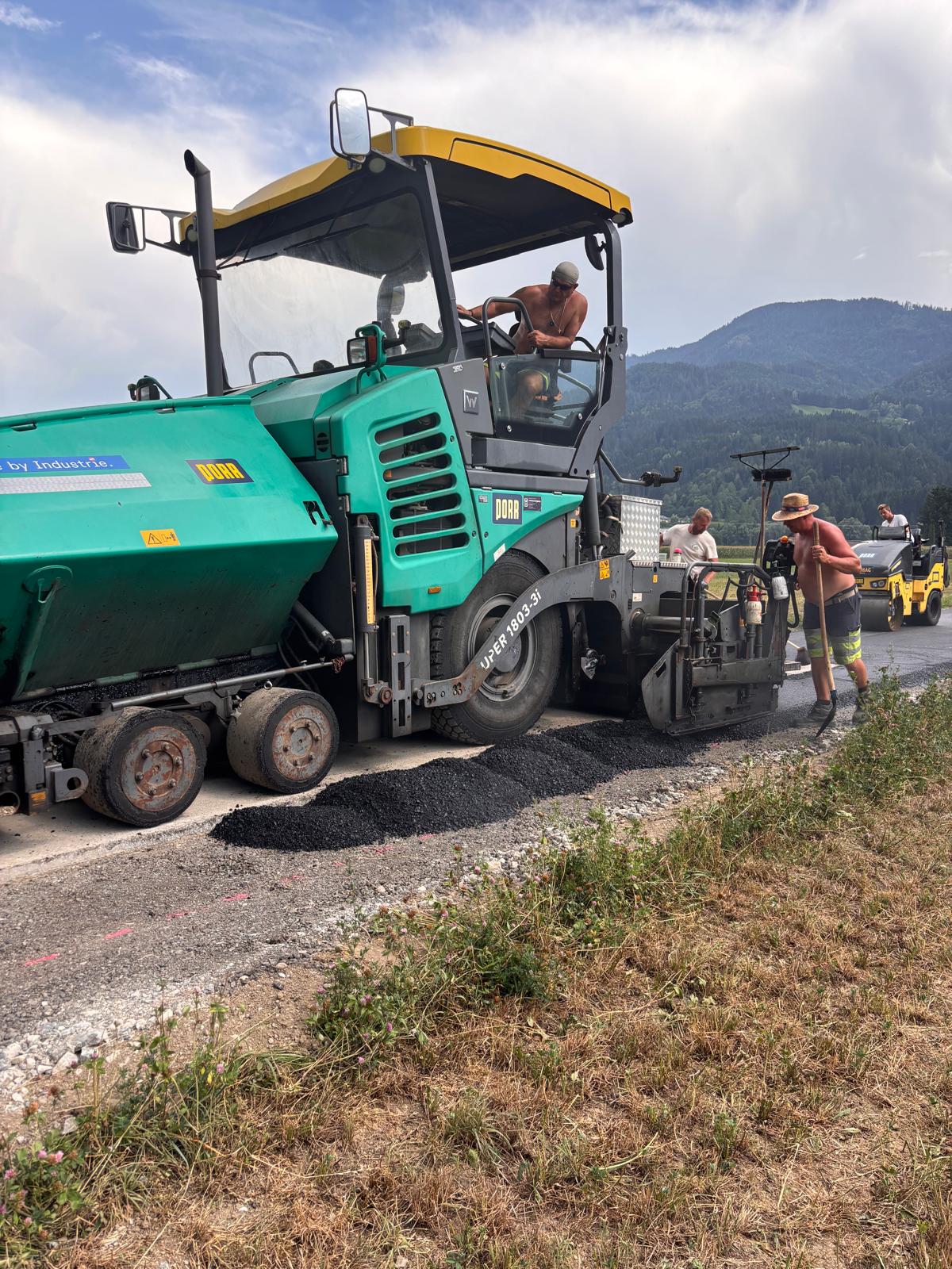 Straßenbauarbeiten mit Asphaltfertiger in Österreich, Arbeiter legen Asphalt, Berge im Hintergrund